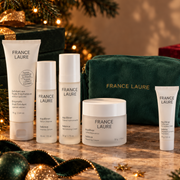 A set of France Laure skincare products arranged on a marble surface with a dark green velvet pouch, holiday greenery, and warm string lights in the background. Balance blemish control holiday gift set for oily skin france laure skincare