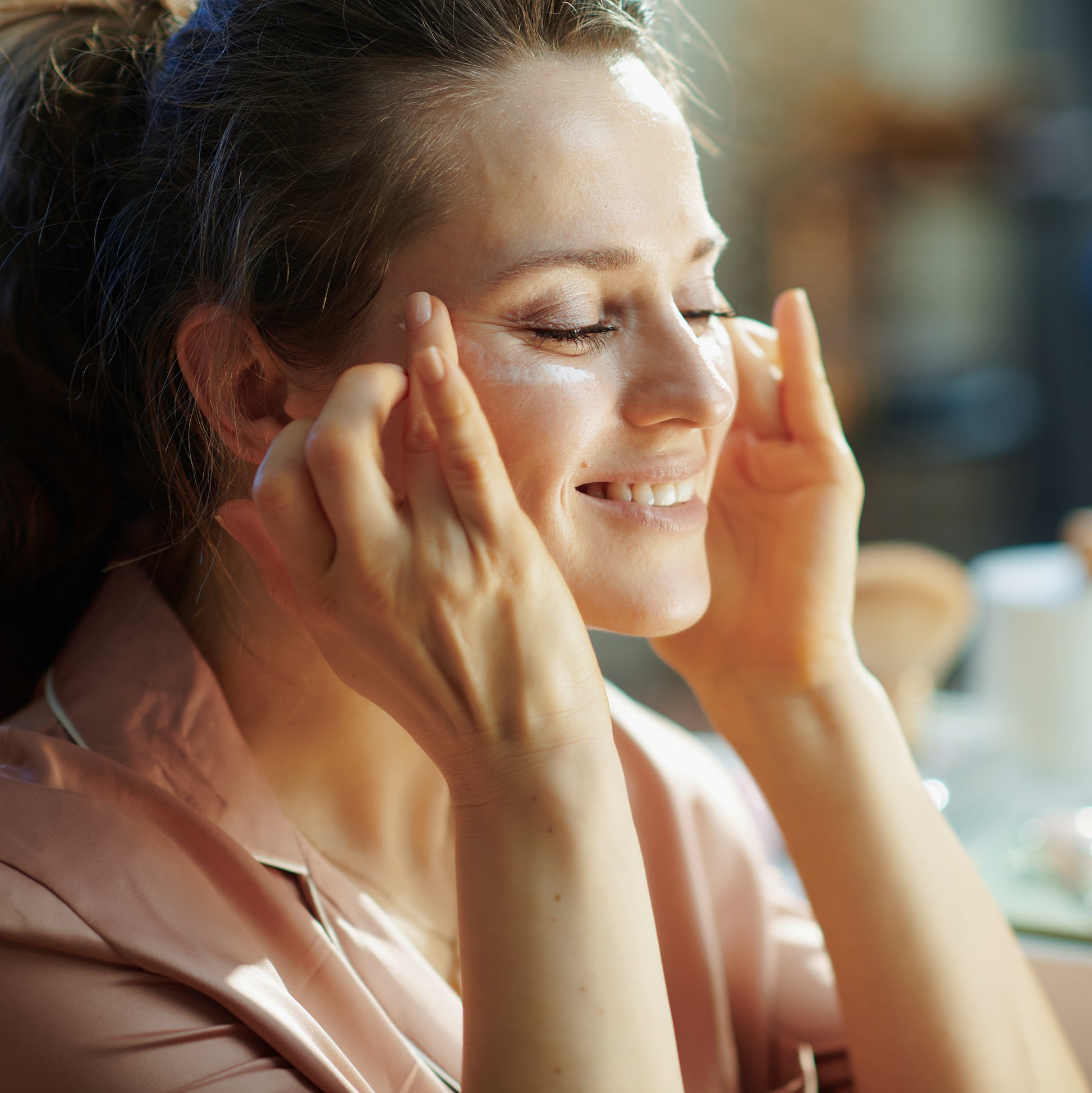 Woman gently applying moisturizing cream to her face, showcasing smooth skin care routine with natural light