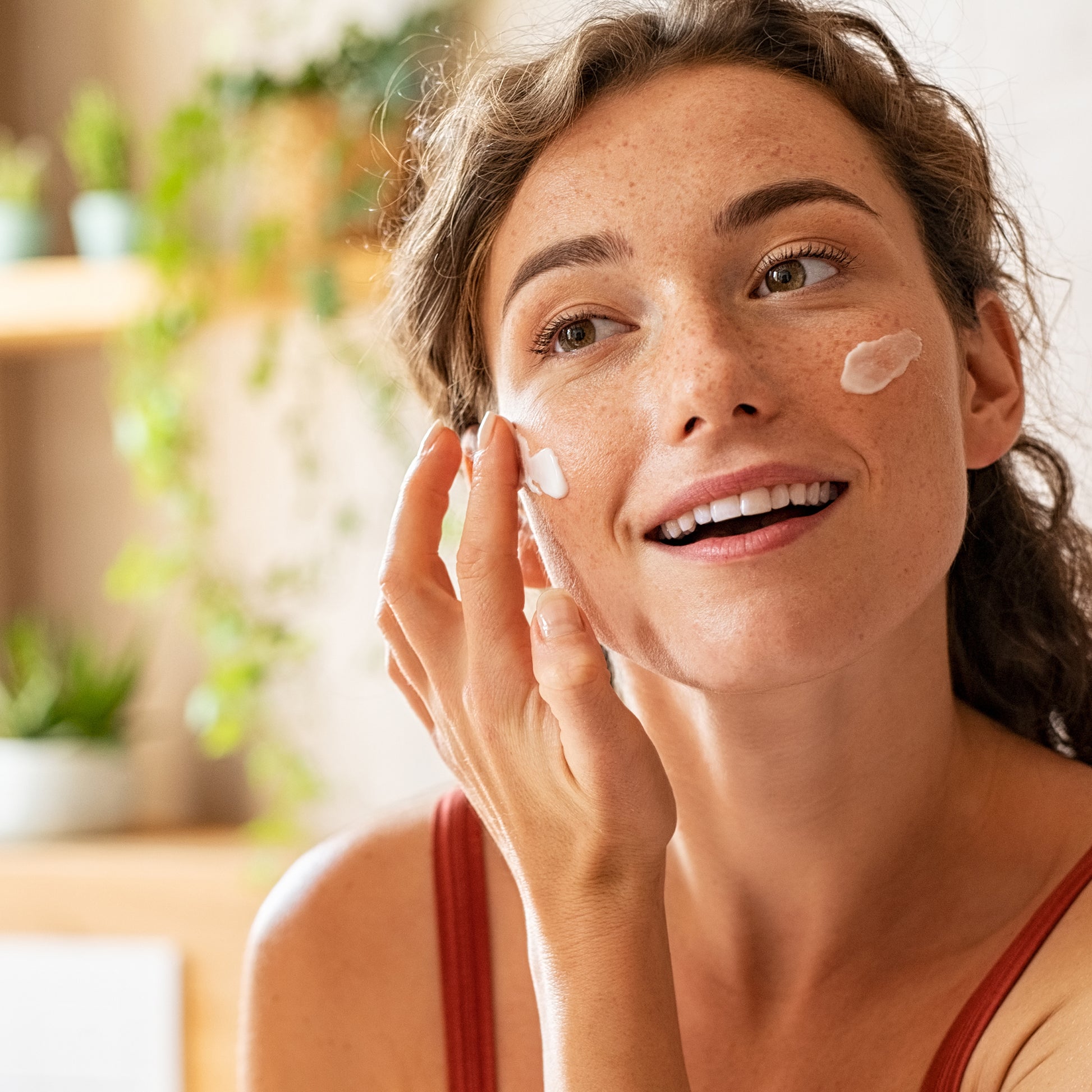 Woman applying gentle face cream to her cheek, showcasing natural skincare routine for all skin types with visible moisturizing texture