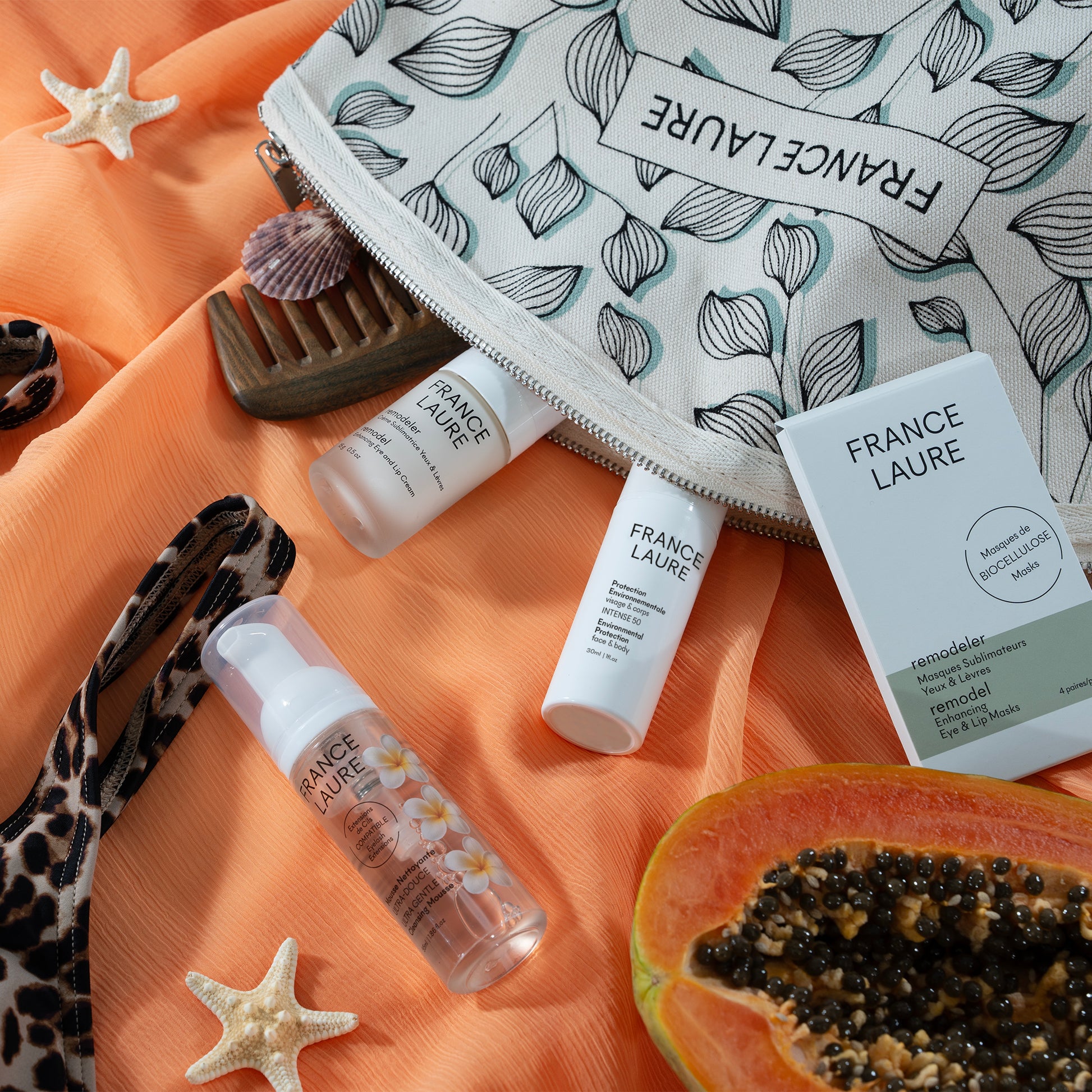 France Laure skincare set with eye & lip masks, environmental protection cream, and gentle cleansing mousse on orange fabric with starfish and papaya